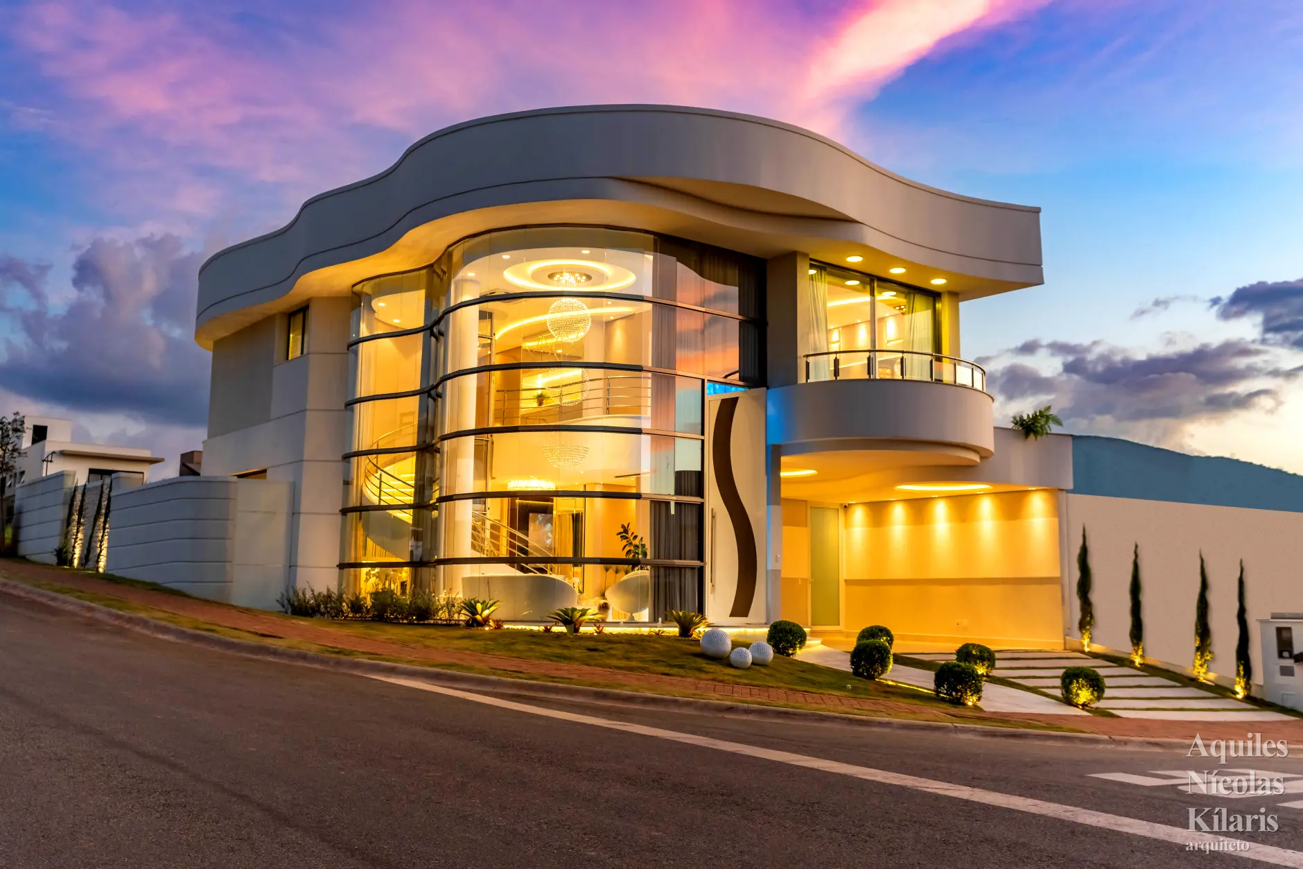 Residência iluminada ao anoitecer com marquise fluida e fachada envidraçada